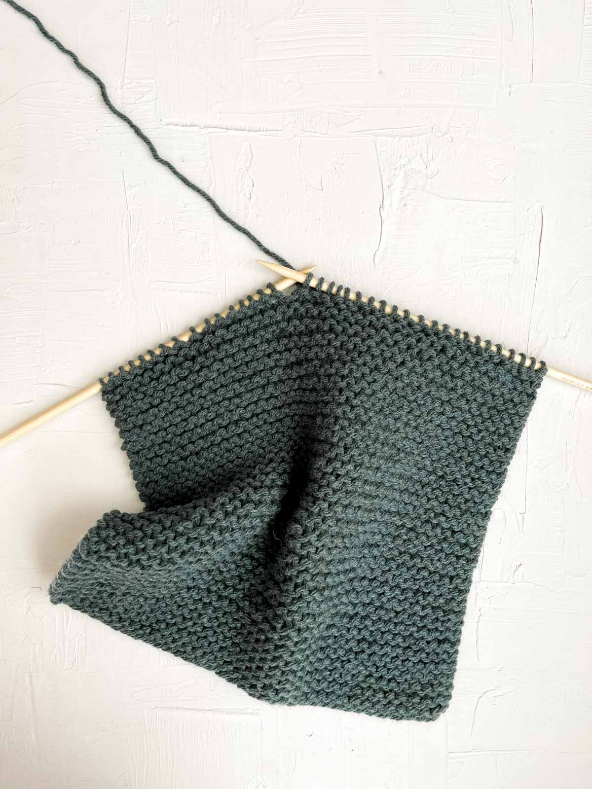 Wooden knitting needles and green yarn making the garter stitch.